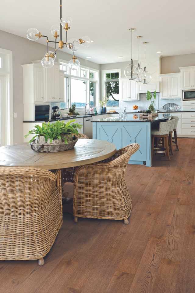 rich hardwood flooring in casual coastal kitchen with blue kitchen island and wicker chairs